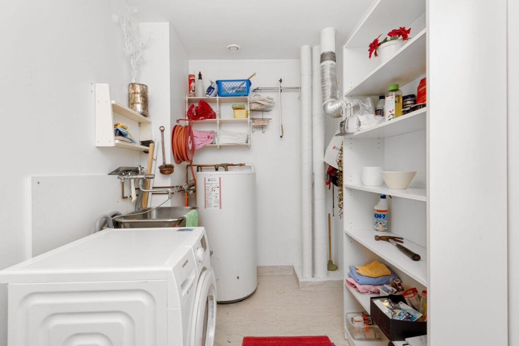 Home laundry room with a washing machine near plumbing and a water heater