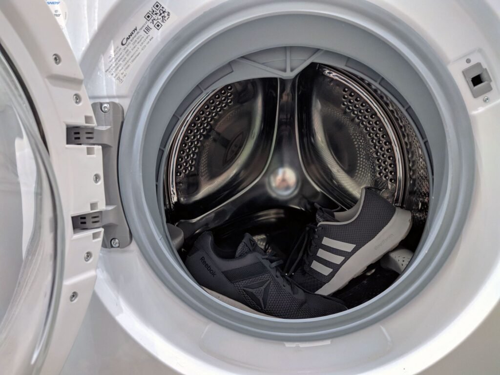 A pair of trainers sitting loose in a front-load washer drum, without the mesh bag that protects the machine