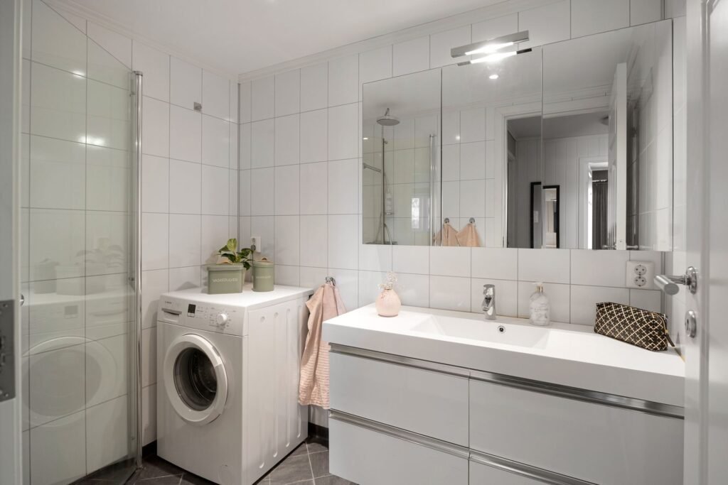 A front-load washing machine in a white tiled room, the form factor that has a drain pump filter to check