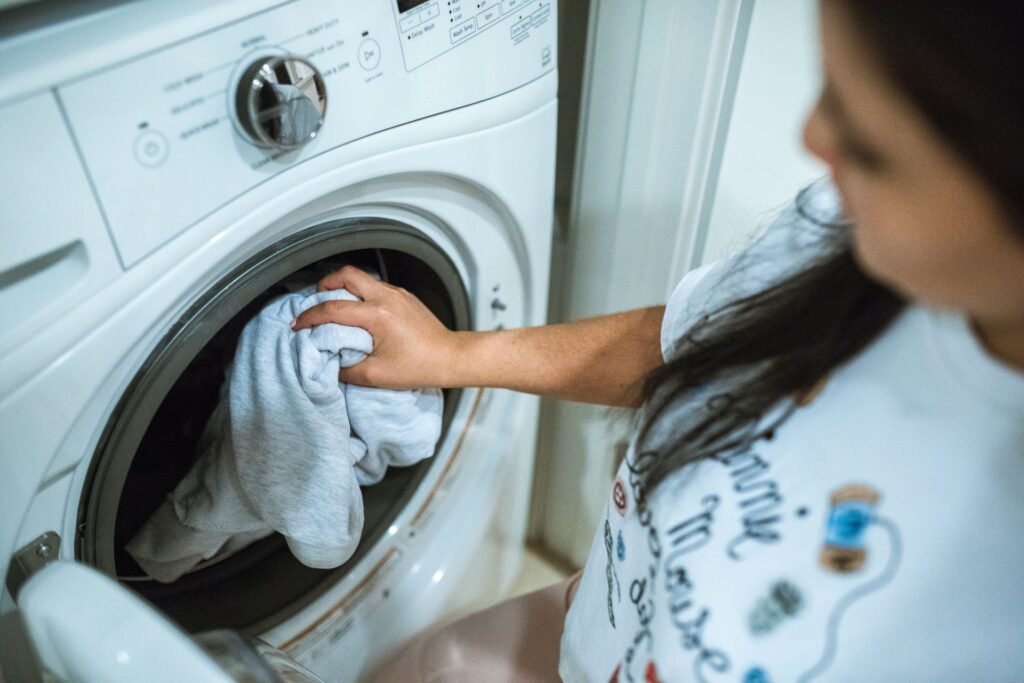 A person loading a front-load washer with the cycle selector dial visible above the door