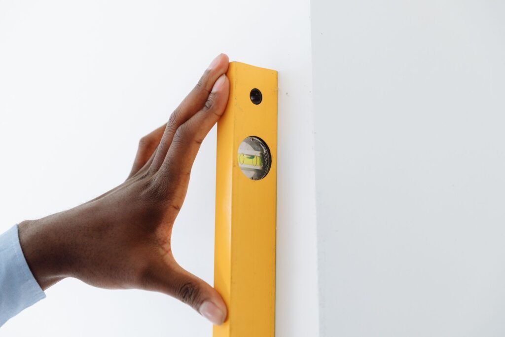 Close-up of a hand using a yellow spirit level against a wall, relevant to confirming a Samsung washer is level after an 8C sensor error