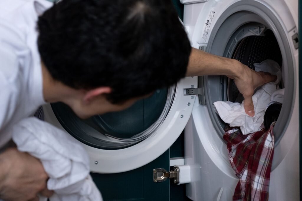 A person pushing a bundle of laundry into a front-load washer drum that is already part full