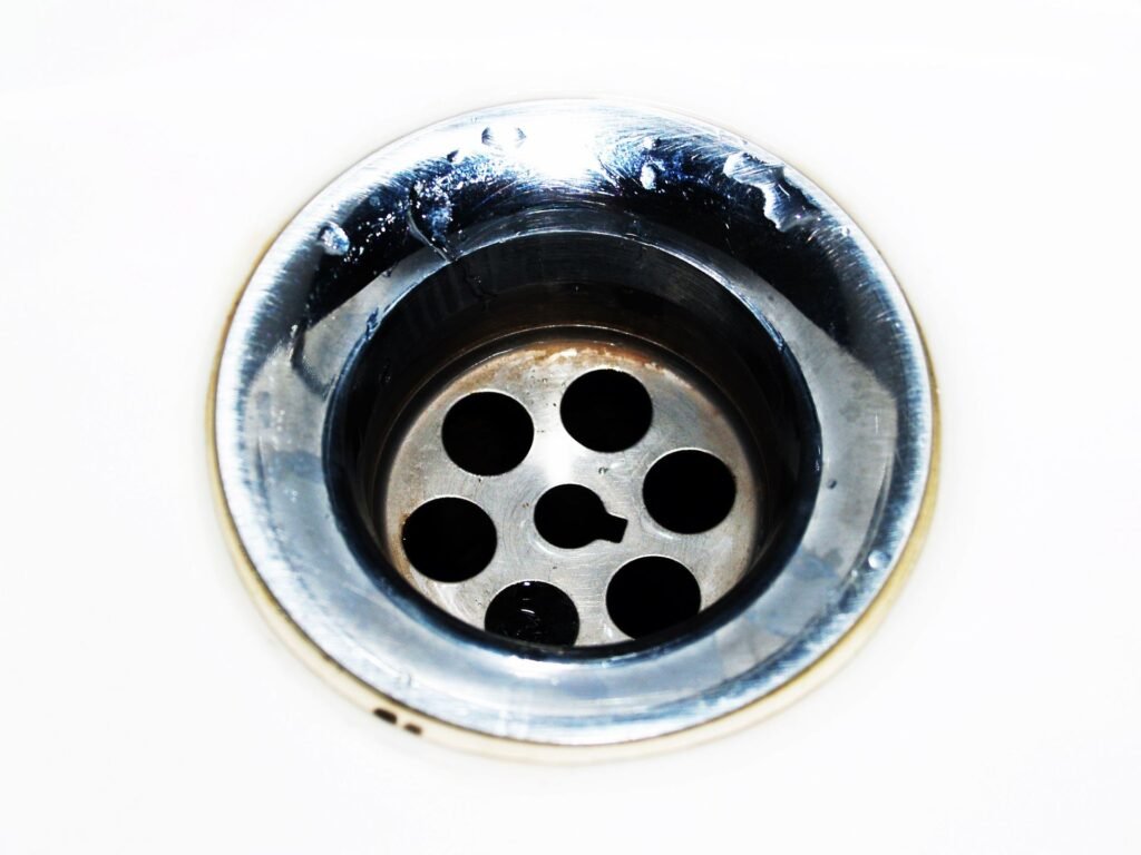 A drain opening with visible grime around the strainer, the kind of build-up behind a washing machine drain pipe overflowing