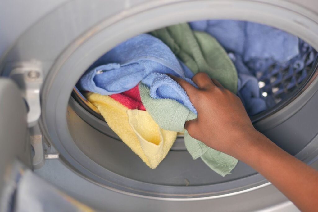 A hand loading folded bath towels into a front-load washer drum