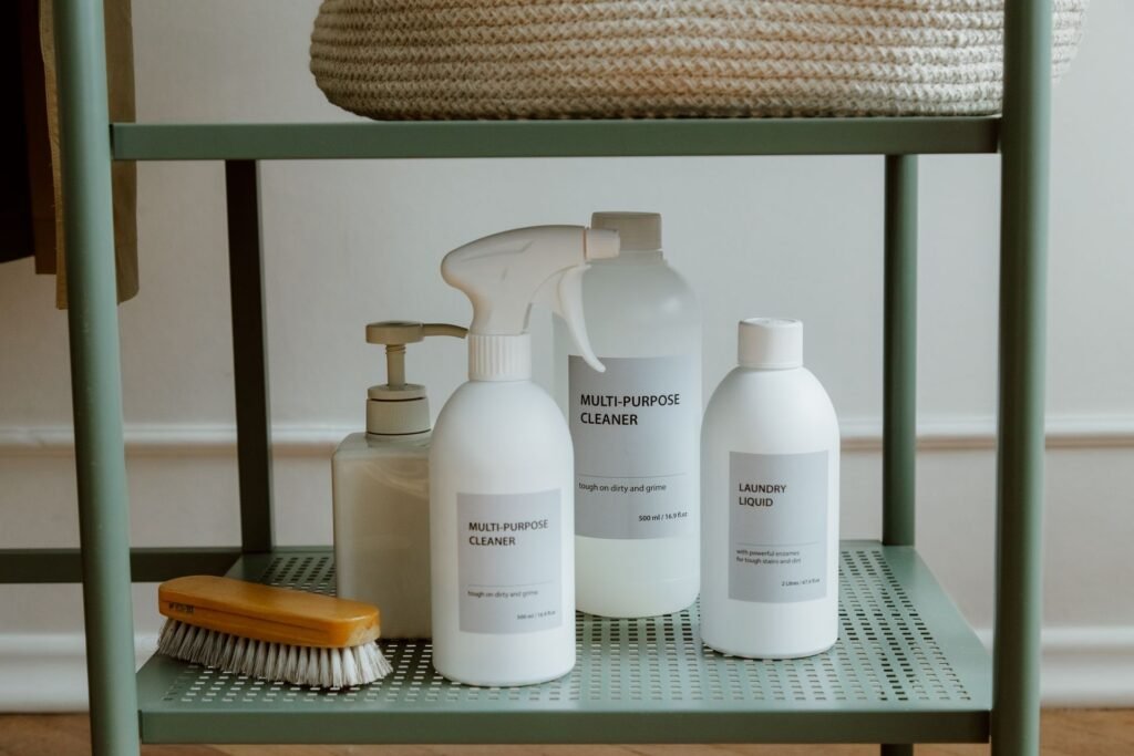 Laundry liquid and cleaning bottles on a shelf beside a laundry brush, the products that go into a washer's dispenser drawer
