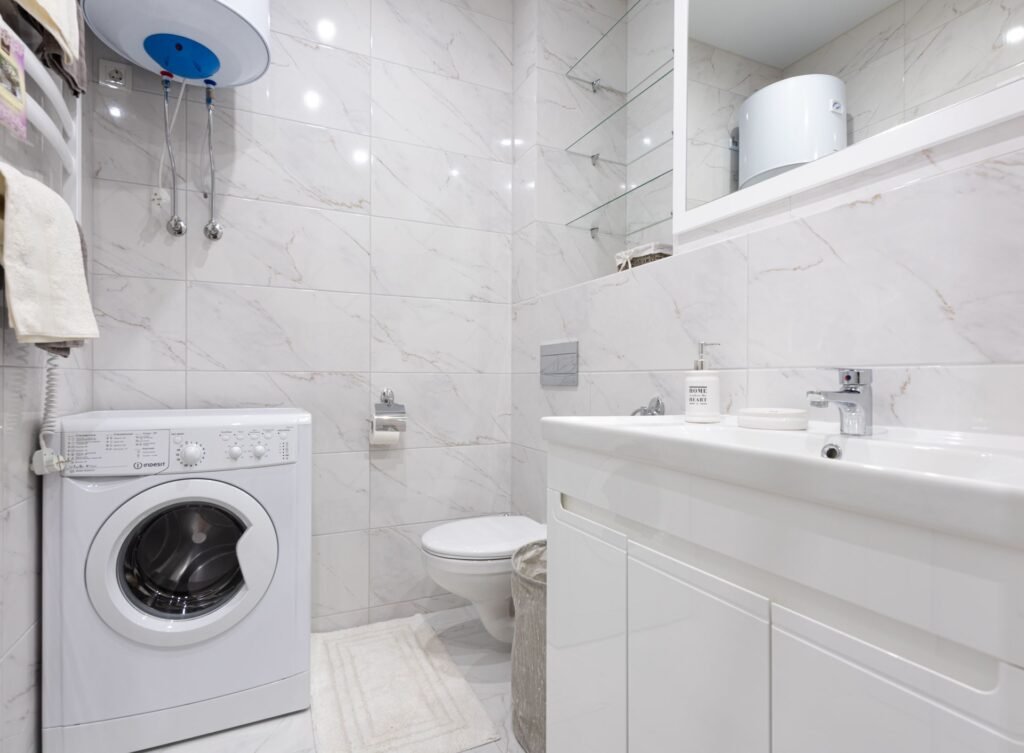 A front-load washing machine standing in a tiled utility space, the kind that refuses to spin on a lid-lock fault
