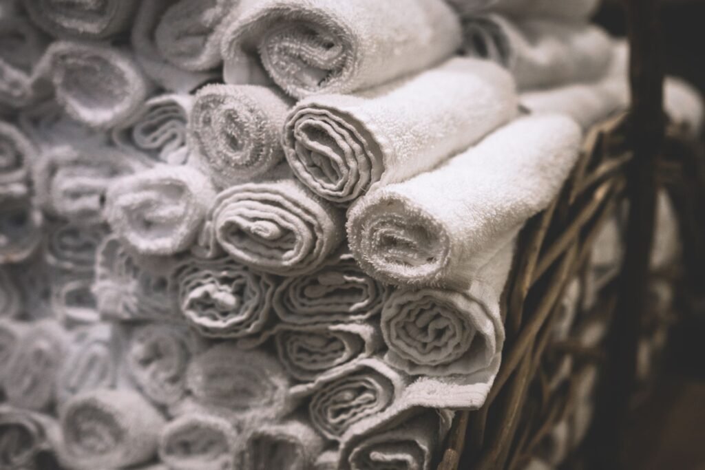 Stack of neatly rolled white towels in a woven basket, relevant to a washing machine white residue on clothes issue