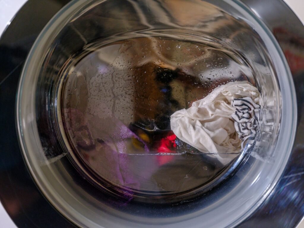 Wet laundry turning behind a front-load washer door mid-cycle, the point at which the machine revises its time estimate