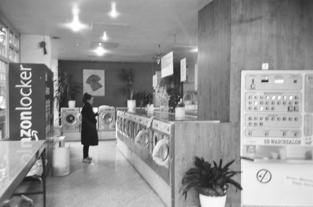 A black and white launderette with a long row of washing machines and a customer waiting beside them