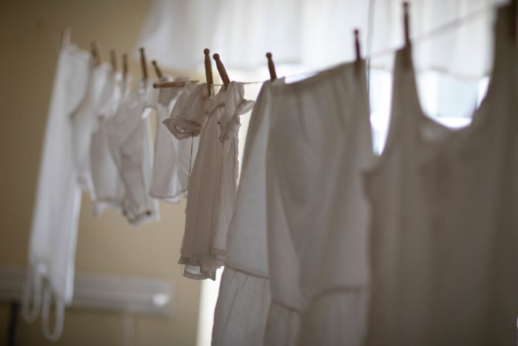 A line of white cotton laundry pegged up indoors in soft light, the wash bleach is meant for