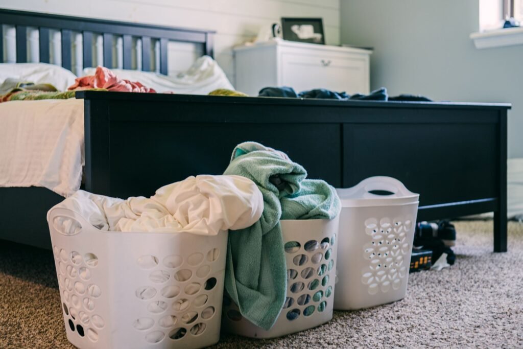 Three laundry baskets piled with clothes beside a bed, the load that has to be washed again