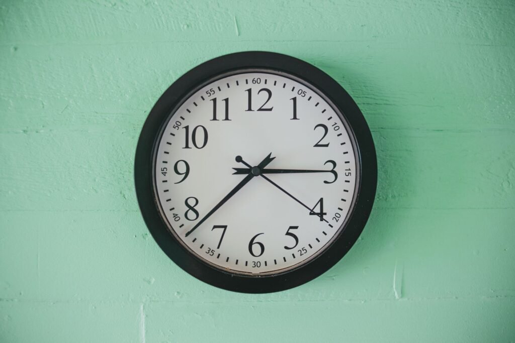 Plain round wall clock on a green wall, the kind of timing a washing machine delay setting is counting towards