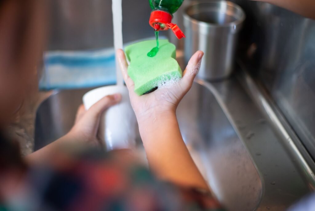 Hand pouring dish soap onto a sponge at a kitchen sink, the job dish soap is actually formulated for