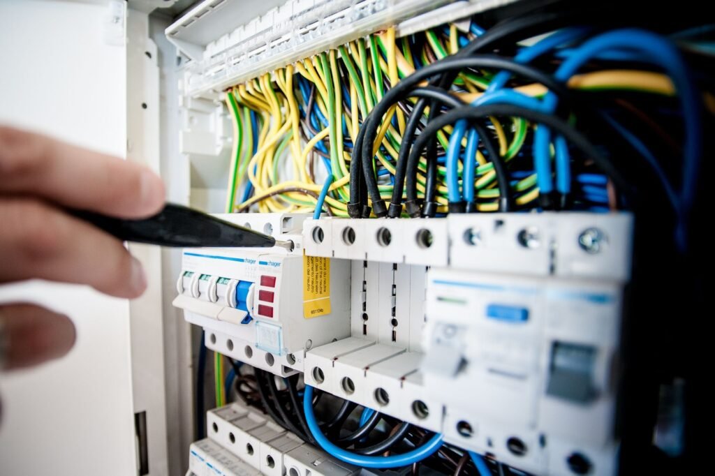 An electrician's hand at an open consumer unit, breakers in a row with coloured wiring behind them