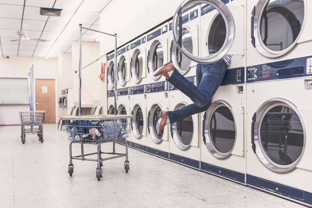An open dryer drum in a laundry room with someone reaching inside, the view after a cycle has stopped before the clothes are dry