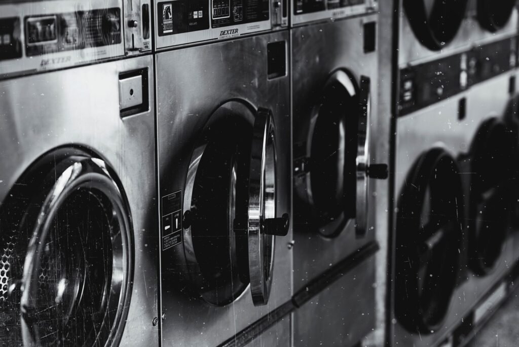 A black and white row of industrial laundry machines with their doors standing open