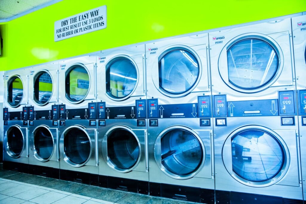 A row of stacked commercial tumble dryers in a laundromat, their drums empty behind round glass doors