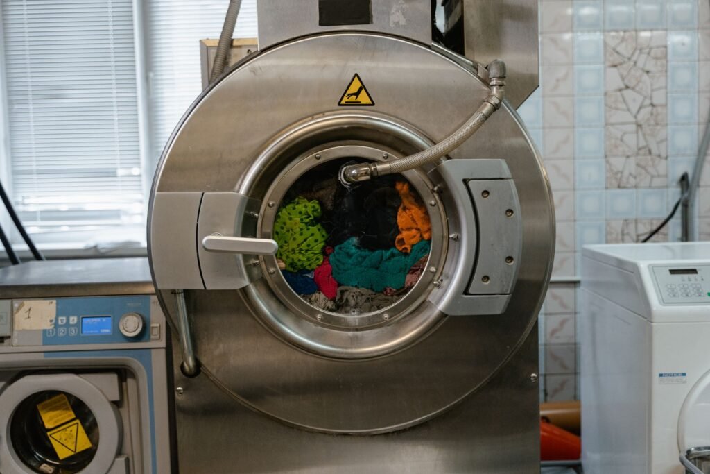 A commercial machine drum loaded with colourful laundry behind a closed steel door