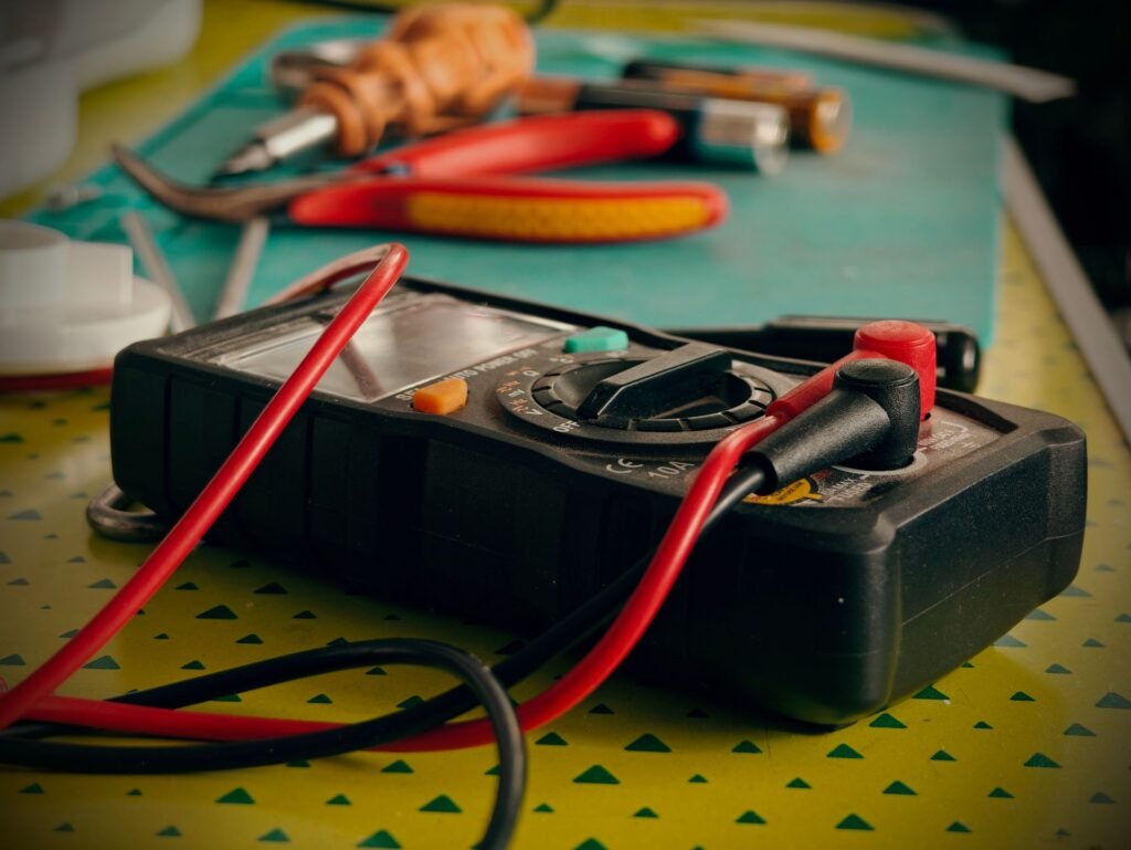 A digital multimeter and hand tools laid out on a workbench, the kit needed to test a dryer thermal fuse for continuity