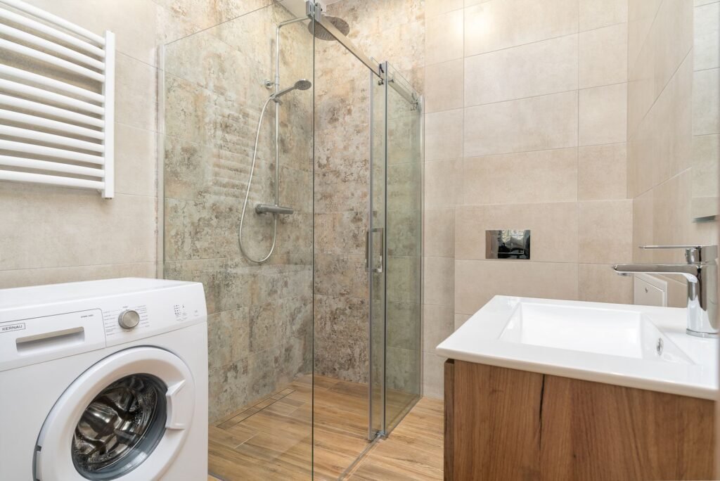 Front-load washing machine with its drum visible, installed against a tiled wall in a bathroom
