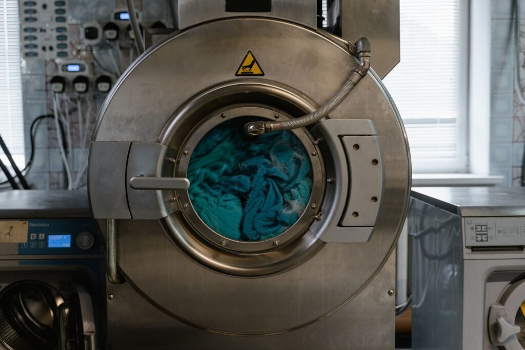 A large front-loading washer with blue fabric visible through the glass and a hose running across the door