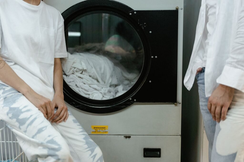 Two people waiting beside a large front-loading machine with white laundry visible through the glass