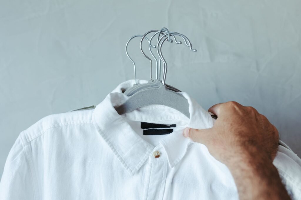 Hand holding up a freshly washed white shirt on a hanger to inspect it for grey marks