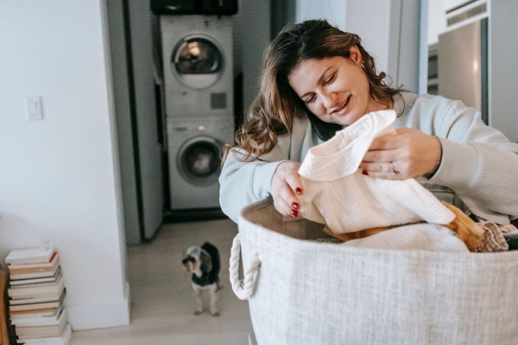 A woman lifting a garment out of a laundry basket in front of a stacked washer and dryer, checking it by smell