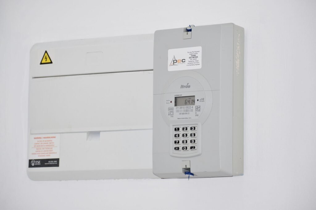 A domestic electricity meter and consumer unit on a white wall, where a washing machine's running cost is actually counted