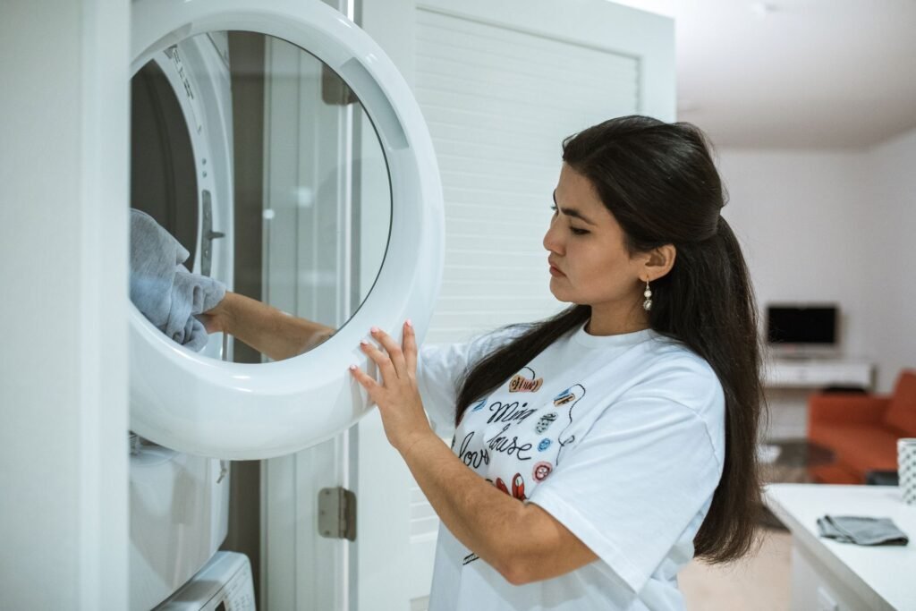 Woman reaching into the drum of a home front-load washing machine with the door open, showing the gasket that needs wiping weekly