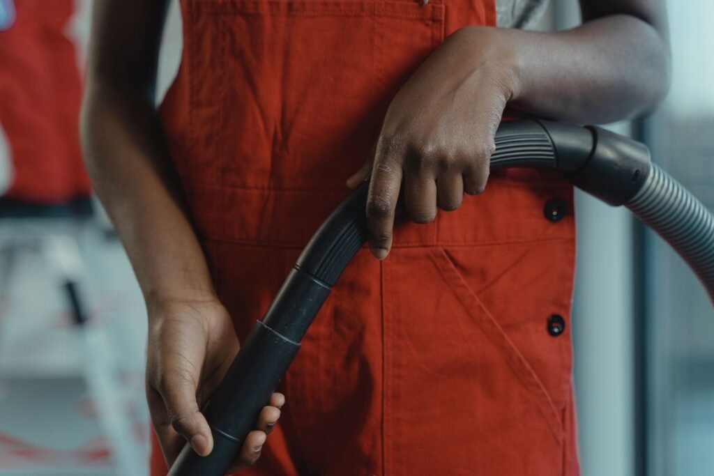 Hands in red overalls holding a vacuum cleaner hose, the tool a lint screen housing actually needs