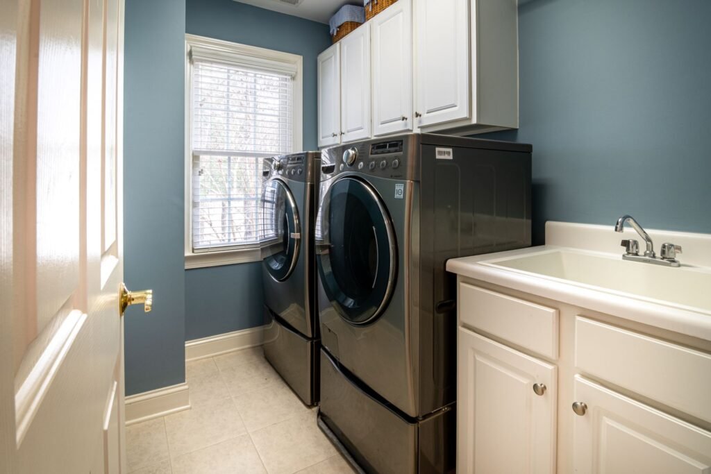 A clean, organised laundry room with a front-load washer and dryer, cabinets and a utility sink