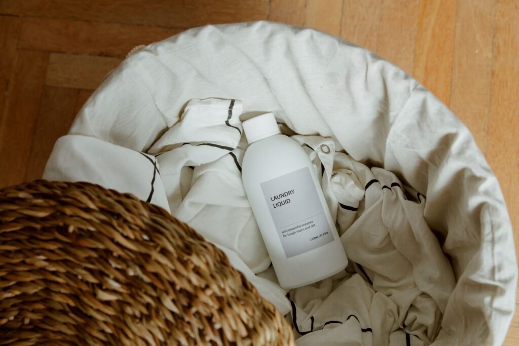 Bottle of laundry liquid resting on white linens in a basket, the product that leaves residue in a washing machine detergent drawer