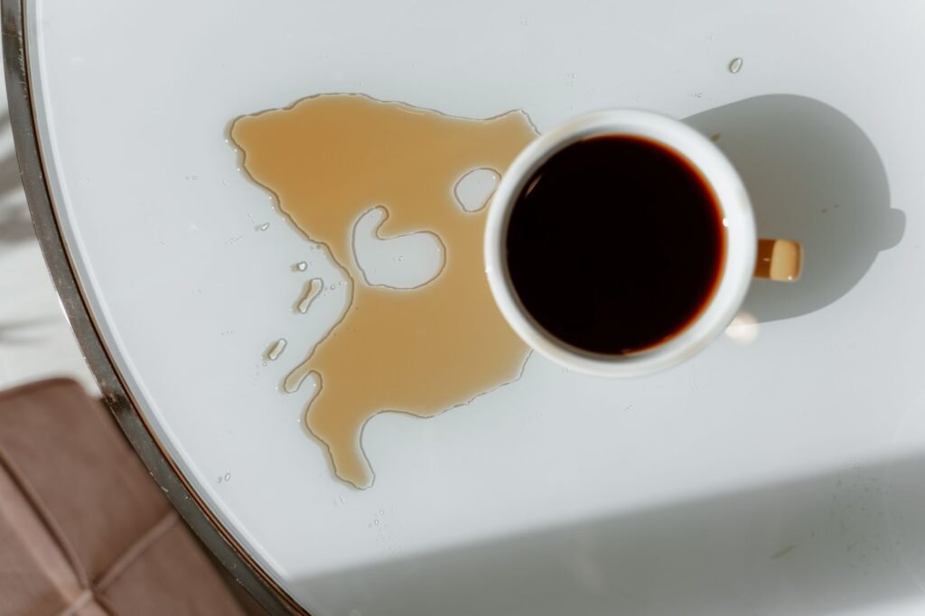 Overhead view of a tipped coffee cup with spilled coffee spreading across a white surface