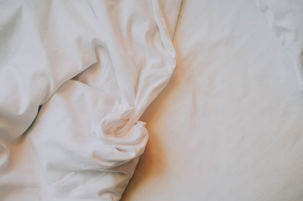Crumpled white bed sheets in soft light, the white cotton where dried blood stains most often turn up