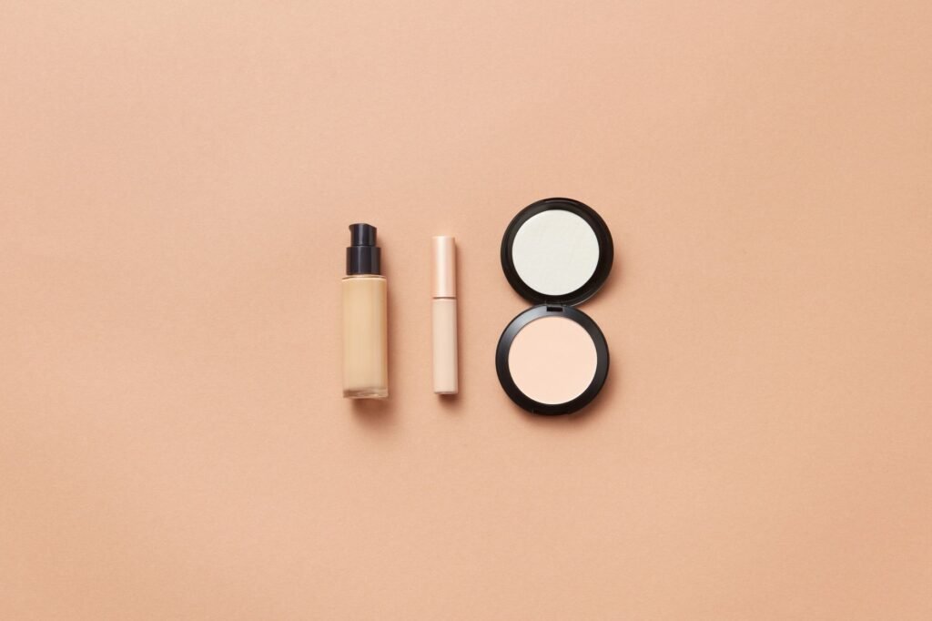 Liquid foundation bottle, concealer and a pressed powder compact arranged on a beige surface