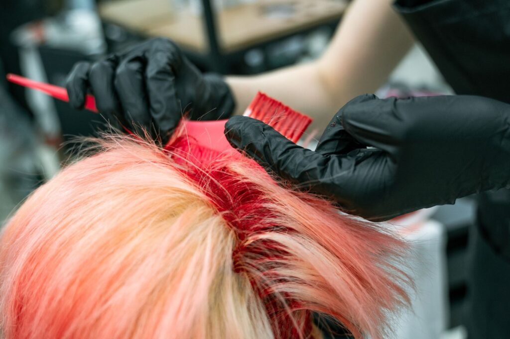 Gloved hands applying hair colour with a tint brush, the stage where most hair dye stains on clothing happen