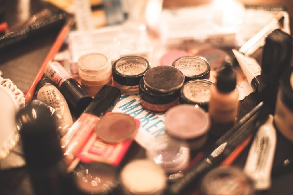 Assorted cosmetics including eyeshadow palettes, lipsticks and brushes spread across a table