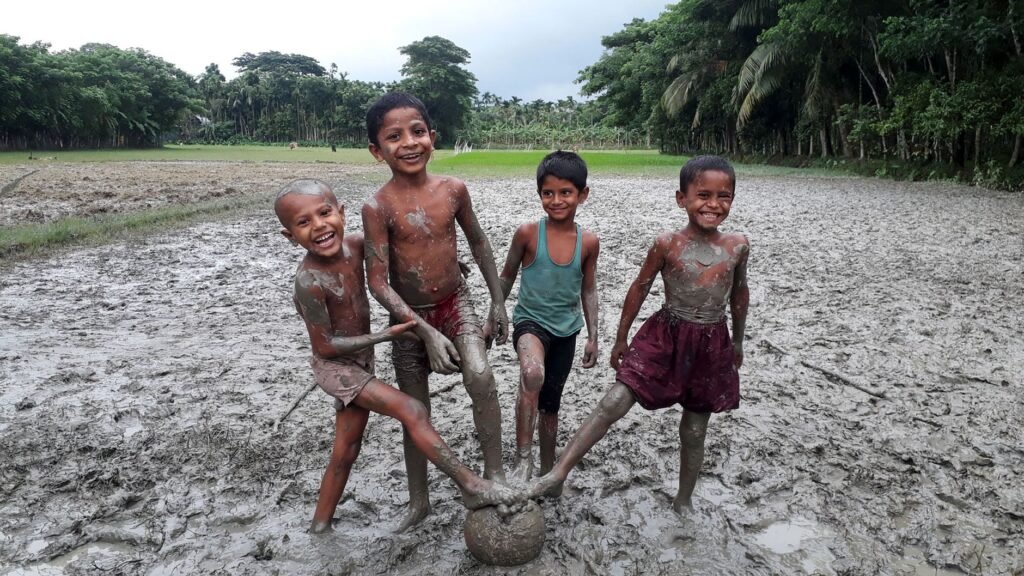 Children covered in mud playing football on a wet field, the usual source of heavy mud stains on kit