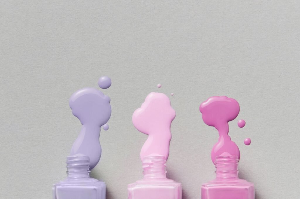 Spilled nail polish pooling on a grey surface beside open bottles, the accident this stain guide covers