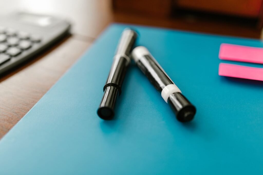 Two black permanent marker pens lying on a blue surface, the pens behind most set-in ink stains on clothing
