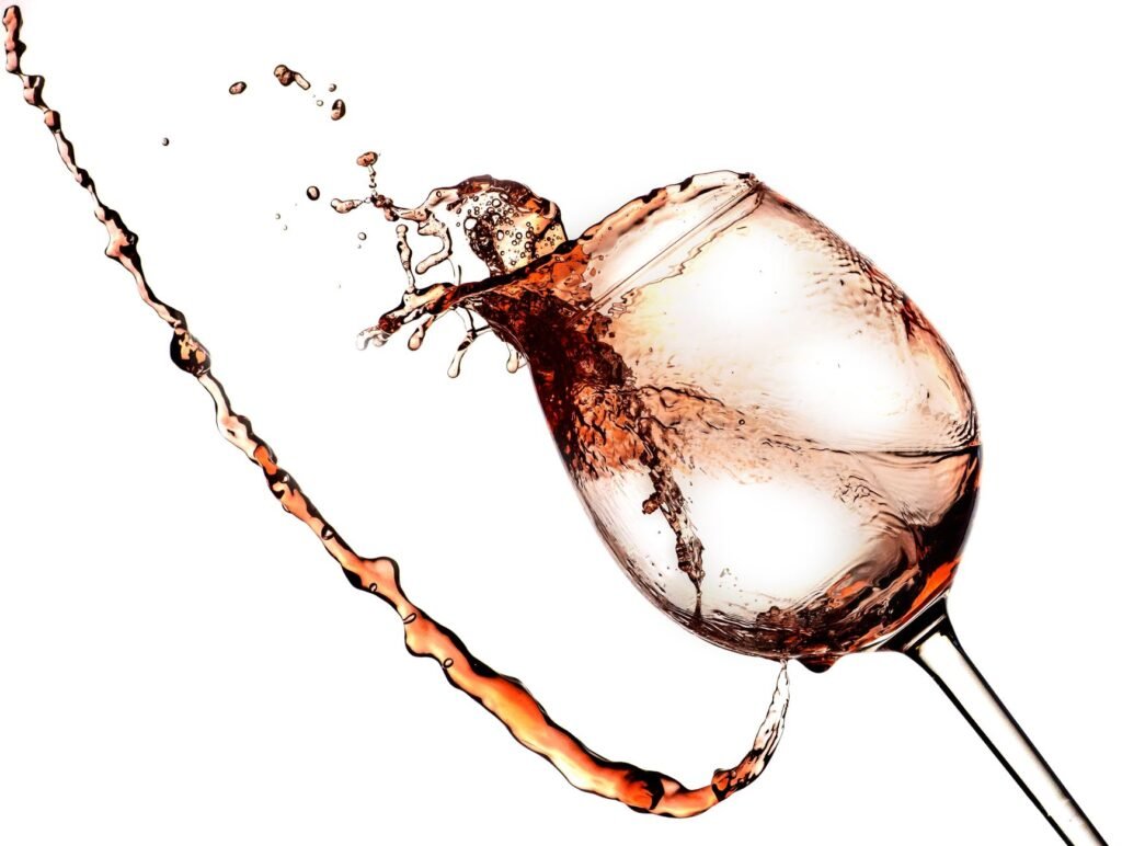 Red wine splashing out of a tipped wine glass against a white background, the moment a wine stain starts