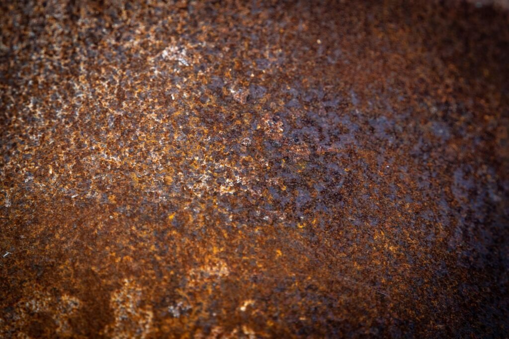 Macro view of a corroded iron surface showing orange rust, the iron oxide that leaves the same marks on fabric