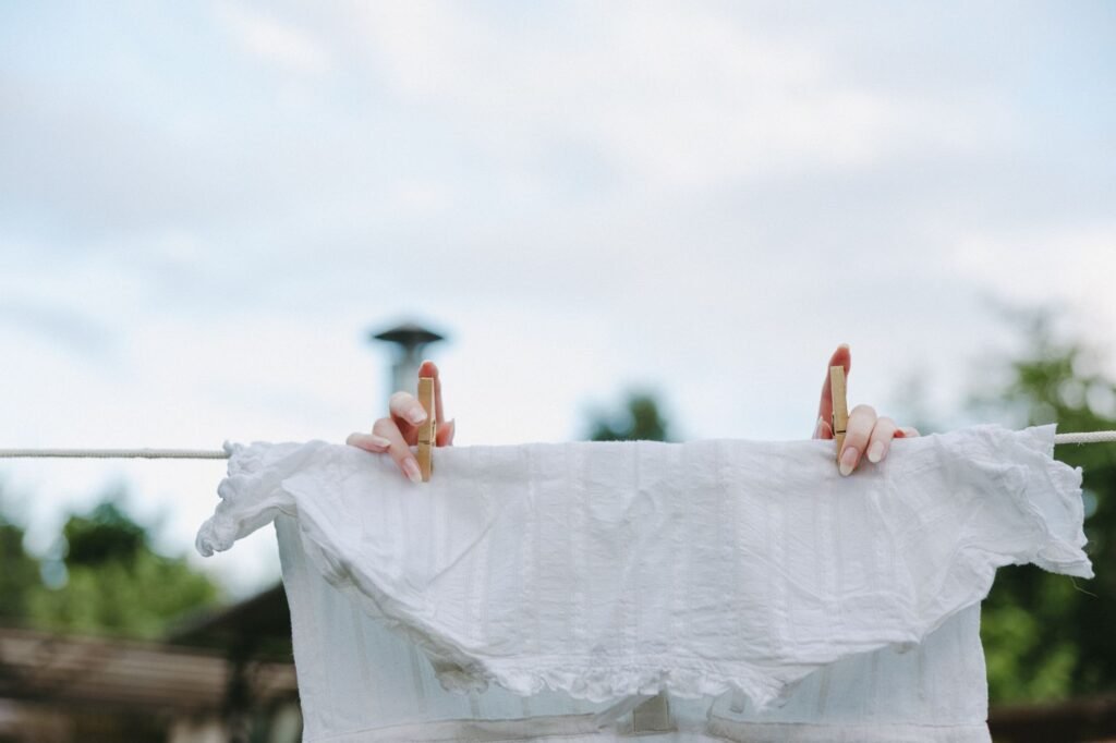 Hands pinning a white blouse to a clothesline in sunlight, the air drying that stops a sweat stain setting