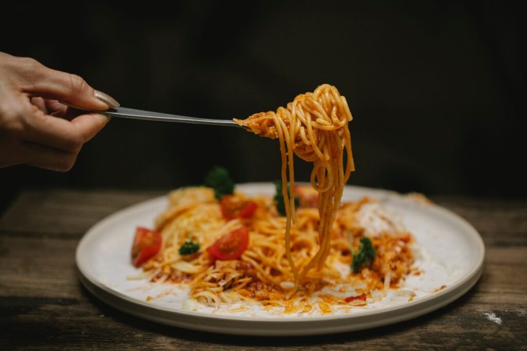 Person eating a plate of spaghetti bolognese with a fork, the everyday moment tomato sauce stains begin