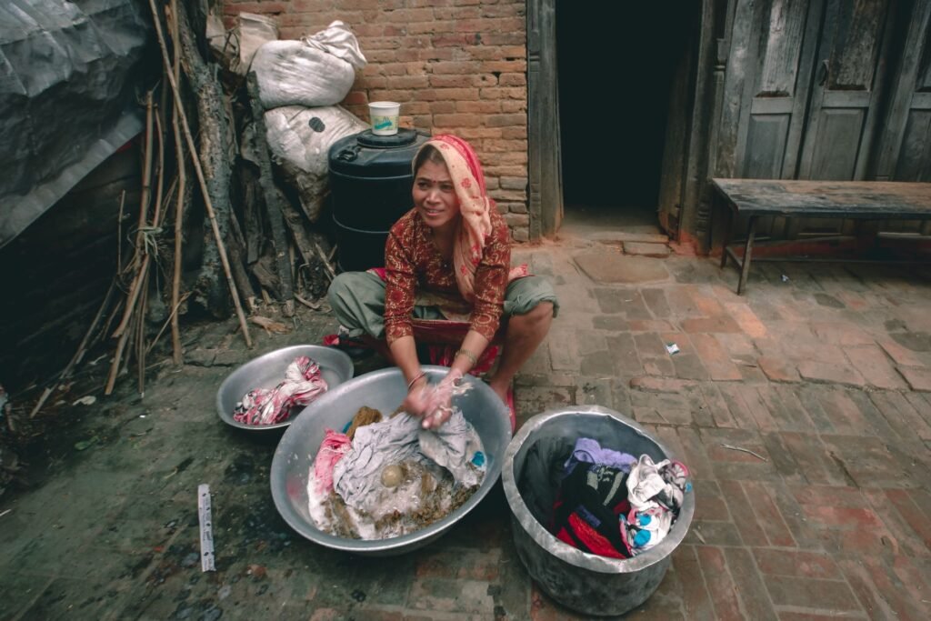 A woman washing clothes by hand in metal basins, working the fabric through the water rather than wringing it