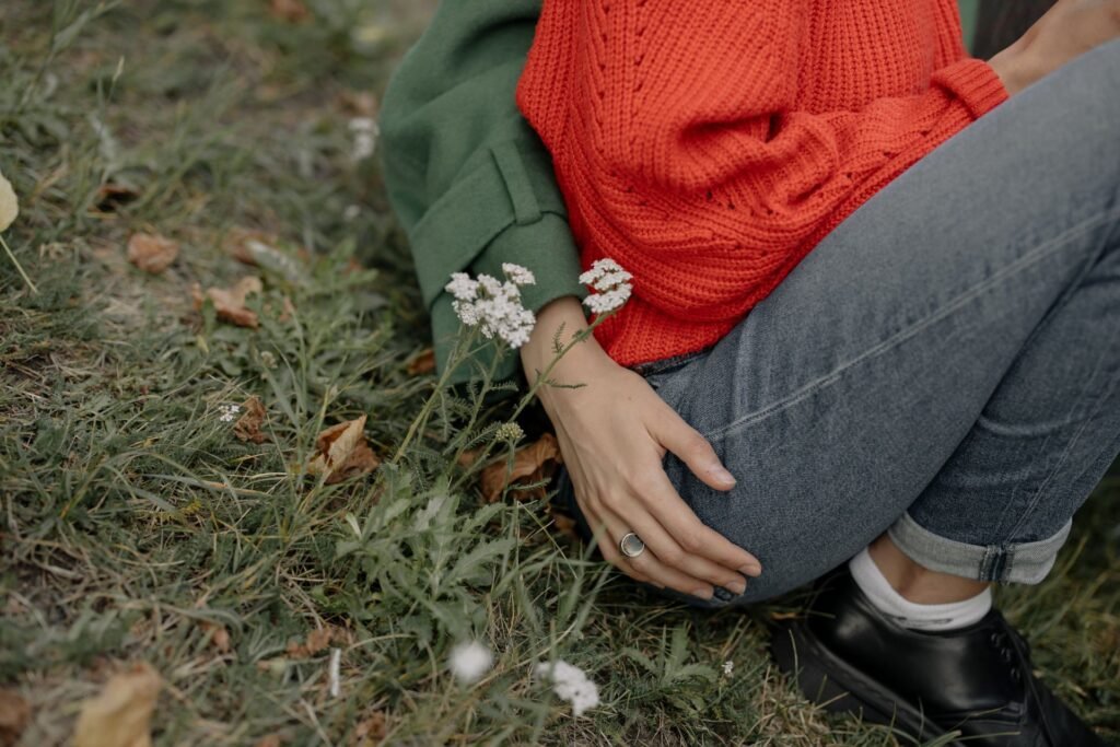 Someone sitting on grass in blue jeans and a red knit jumper, the moment a grass stain is made