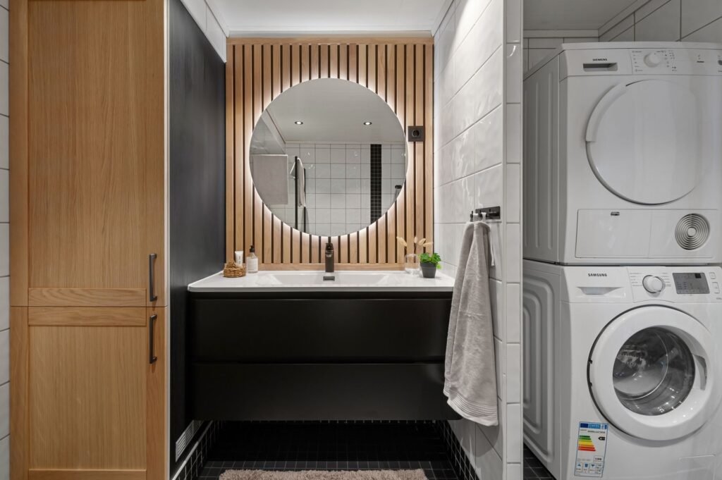 A dryer stacked on top of a front-load washer in a narrow bathroom, the arrangement a stacking kit holds together