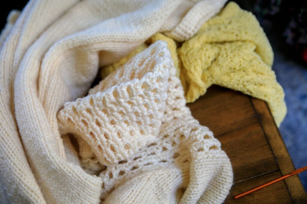 Folded wool knit sweaters in neutral tones on a wooden table, the knitwear that felts if washed wrongly
