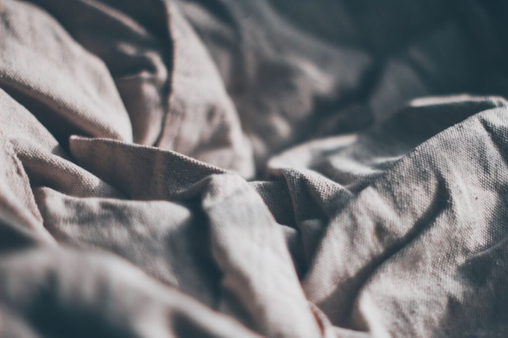 Close-up of creased natural linen fabric showing the loose flax weave and the soft folds it holds
